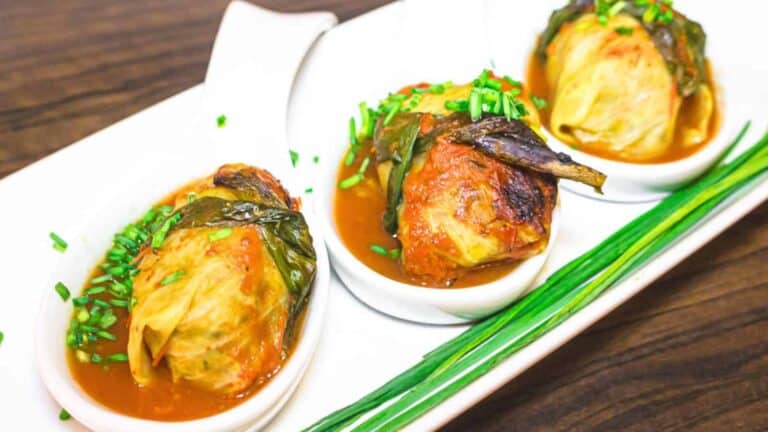 Three plates of cabbage rolls with sauce on a white plate.