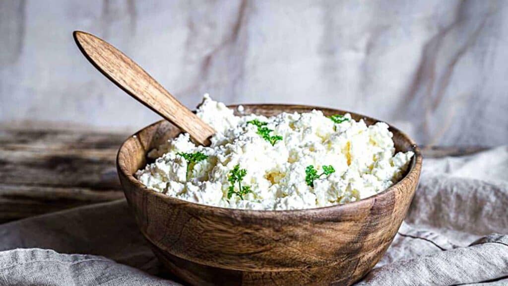 Farmers Cheese in a wooden bowl with herbs on top.