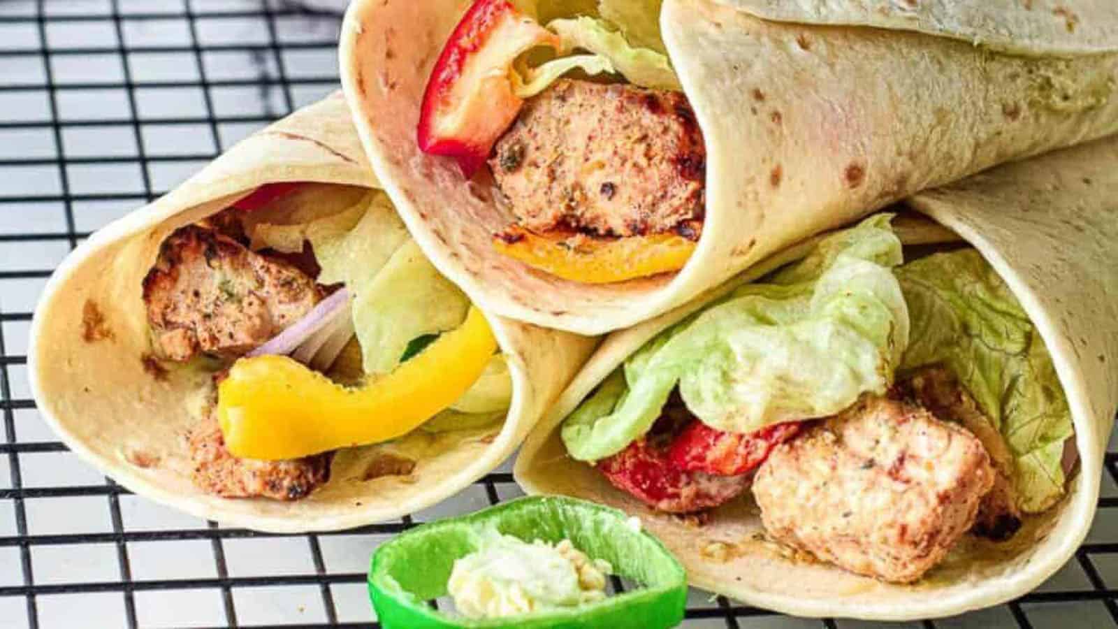 Three wraps with meat and vegetables on a cooling rack.