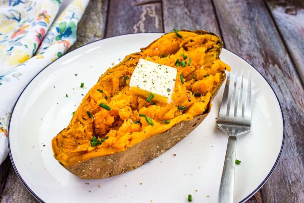 Baked potatoes on a serving dish with sour cream and fresh parsley.