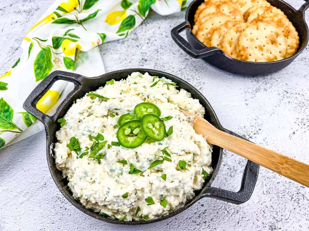 Artichoke Jalapeno Dip in a black bowl with crackers nearby.