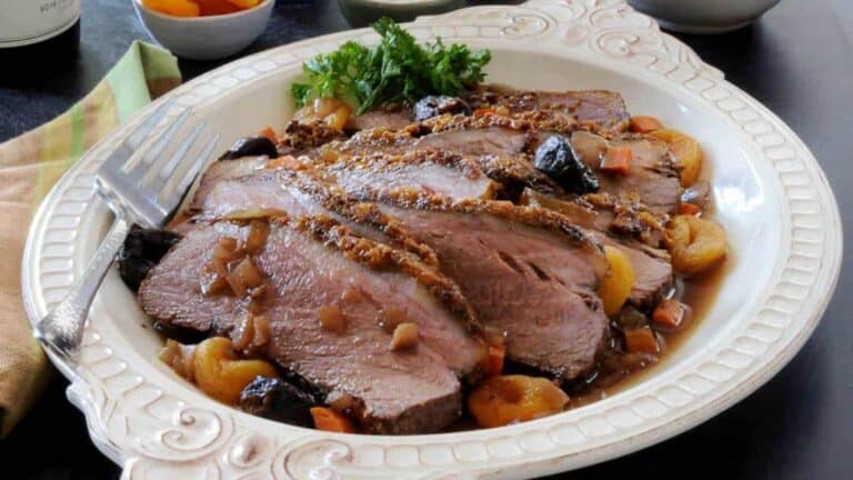 Low angle shot of sliced brisket on a white platter with dried apricots and salt in the background.