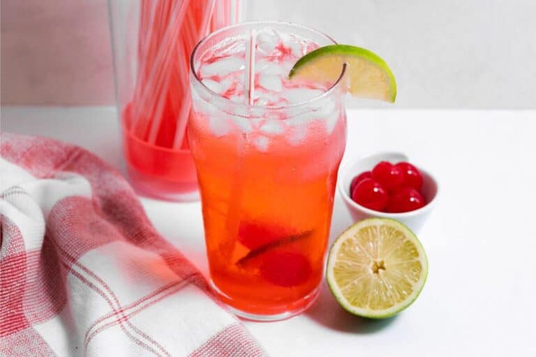 A glass of red drink with lime slices and straws.