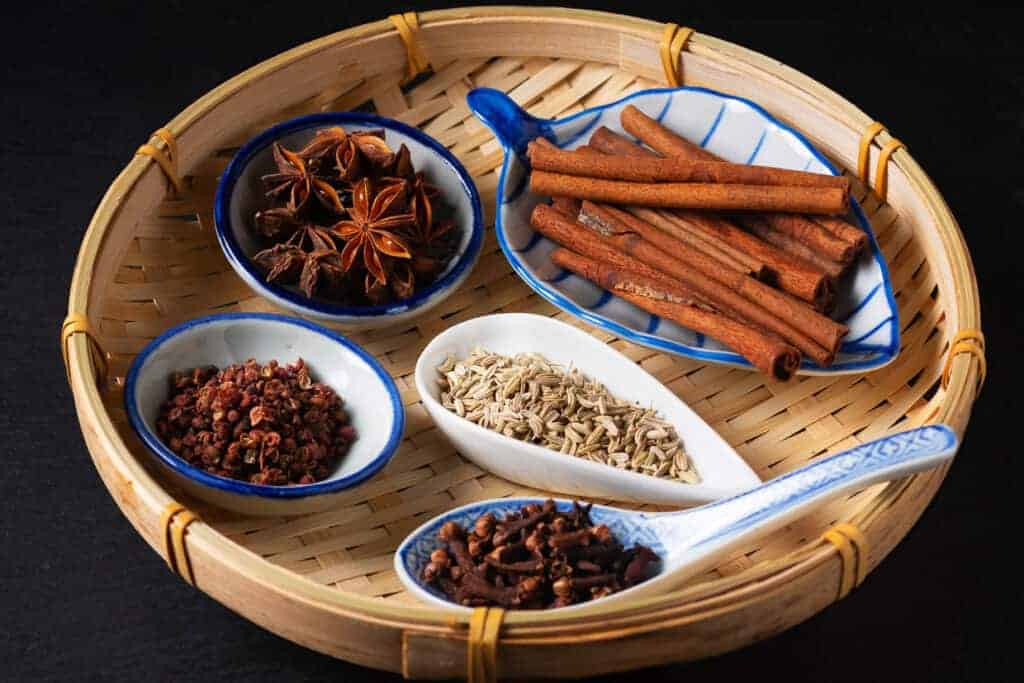Chinese herbs and spices in a bamboo basket on a black background.