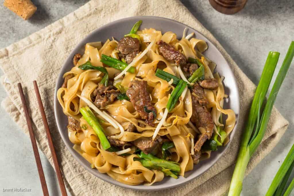 A bowl of beef noodle with green onions and chopsticks.