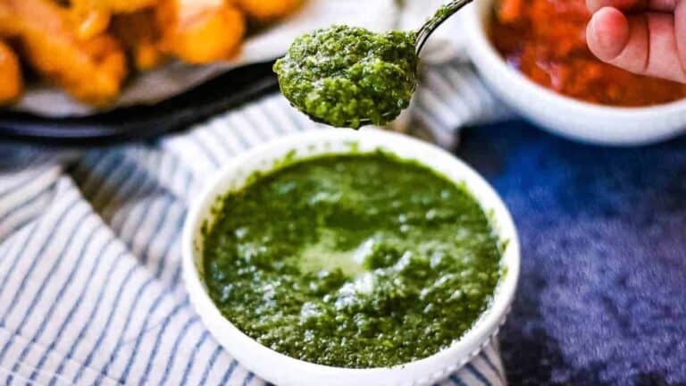 High angle shot of a bowl of cilantro mint chutney with a spoonful being lifted above the bowl.