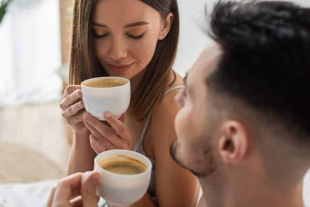 A man and woman drinking coffee in bed.