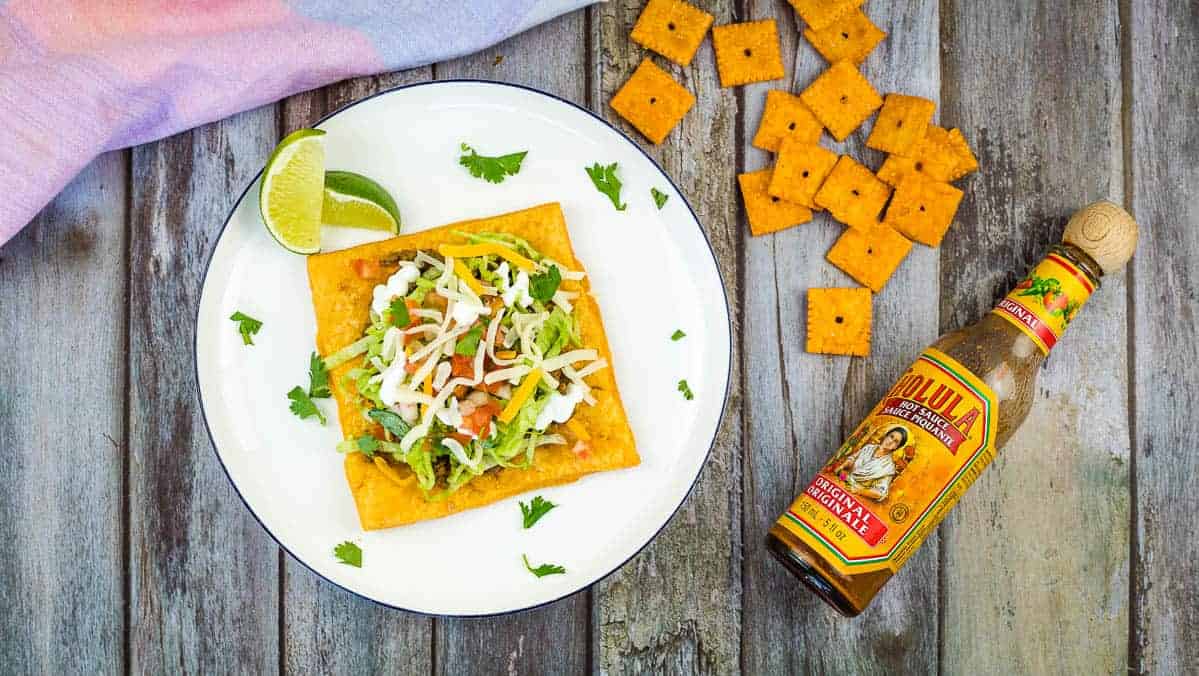 A top-down shot of a Cheez-Its Tostada with crackers and a bottle of hot sauce.