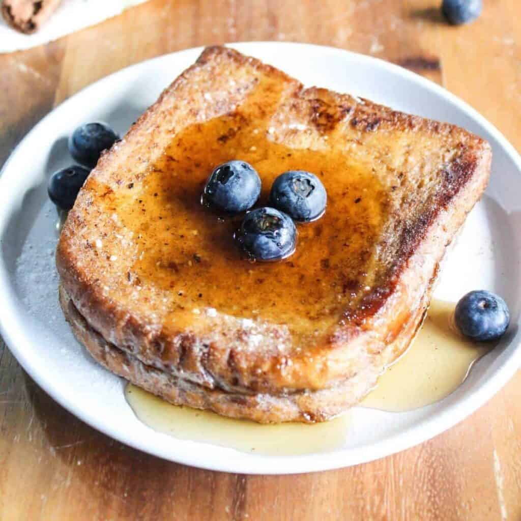 Air fryer French toast slices with syrup and blueberries on plate.