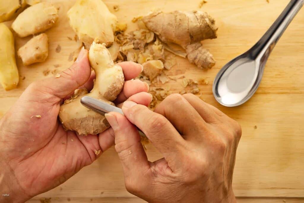 A person is slicing a piece of ginger with a spoon.