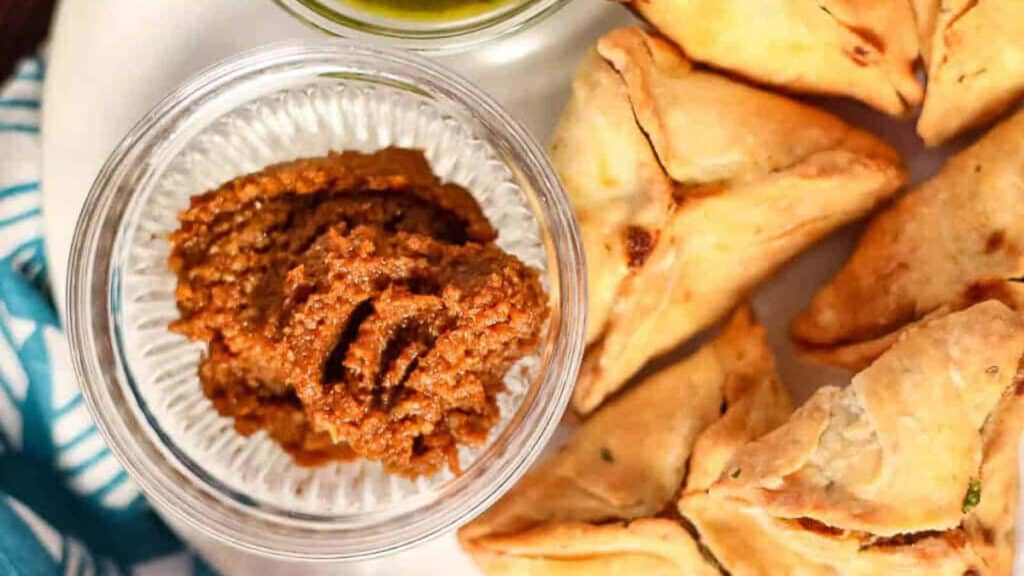 A plate with a bowl of samosas and a bowl of chutney.