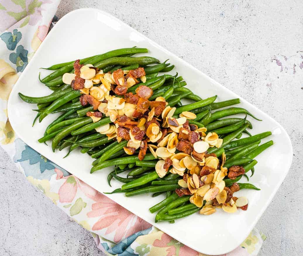 Green bean almondine with bacon on a white platter.