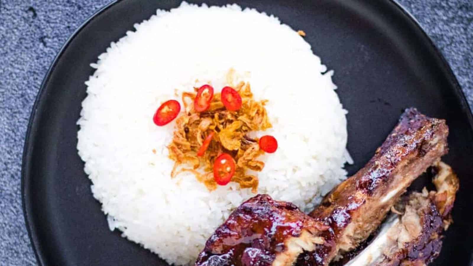 A mound of coconut rice on a black plate with ribs on the side.