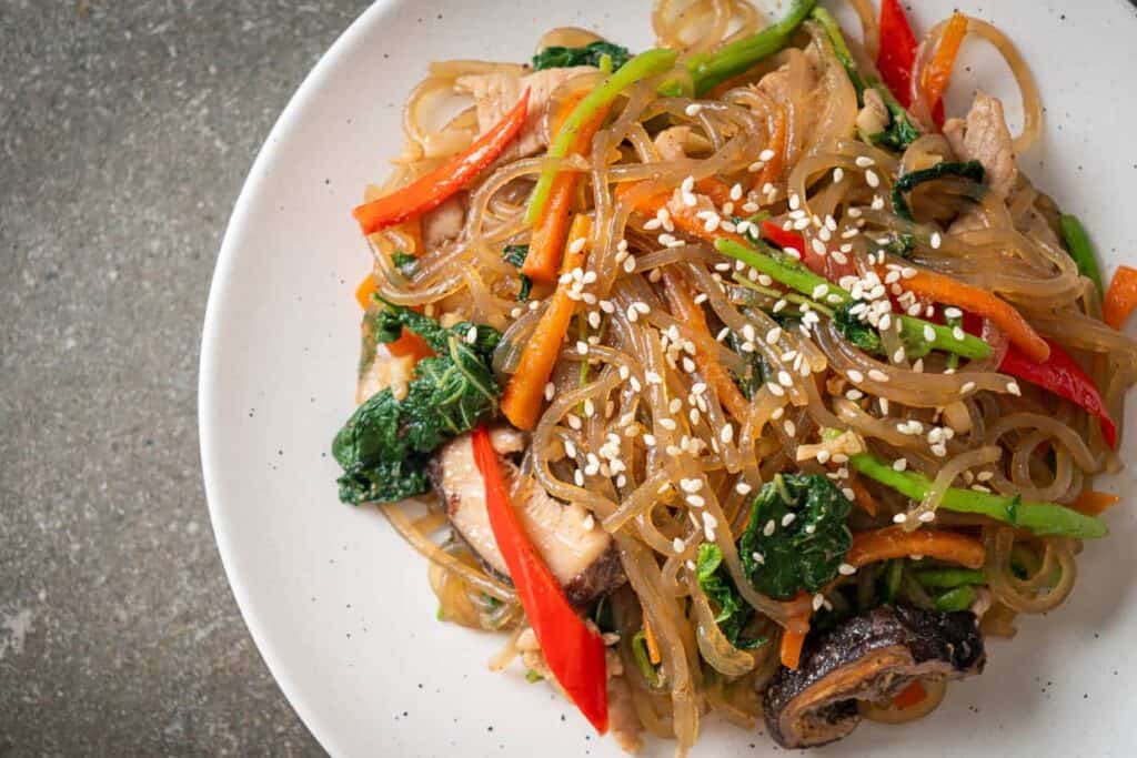 A plate topped with noodles, vegetables and sesame seeds.