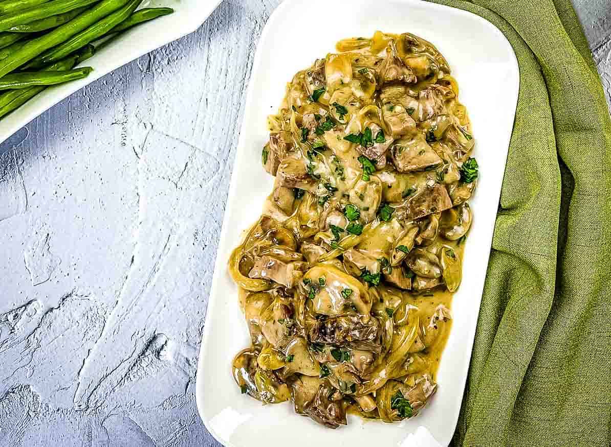 Leftover roast beef stroganoff on a plate with green beans in the background.