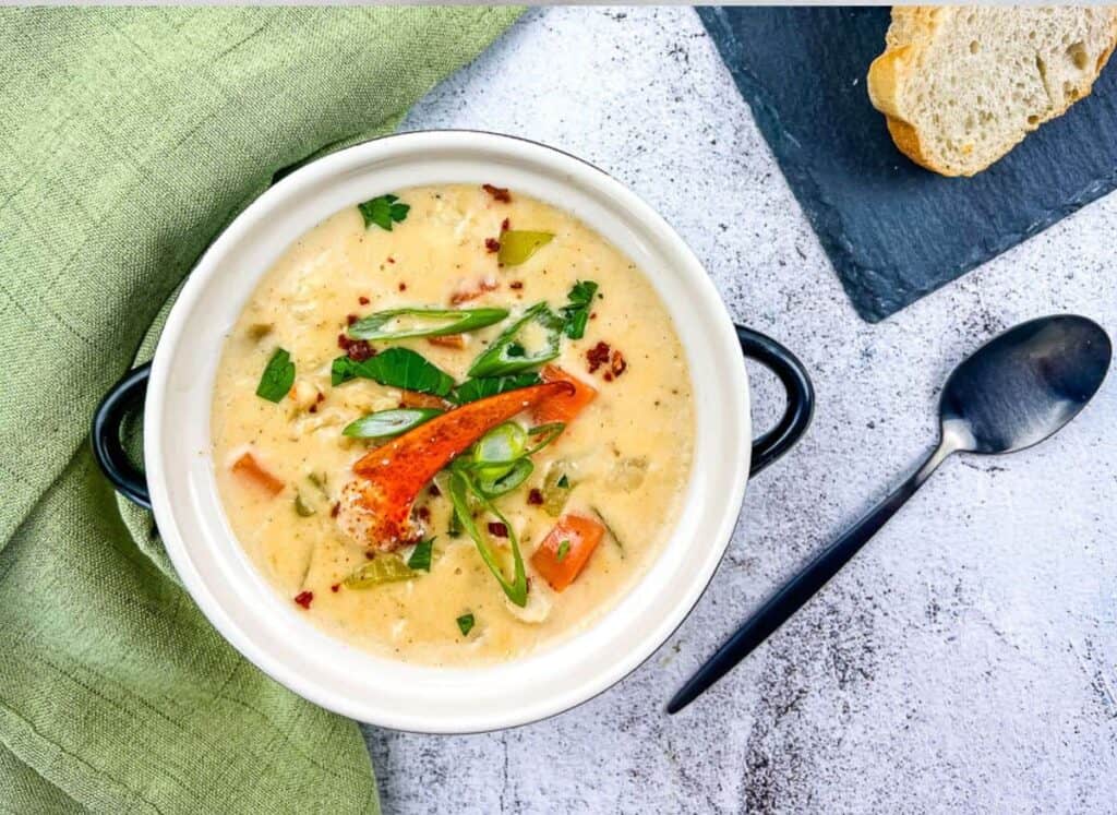 A bowl of lobster chowder with bread on the side.