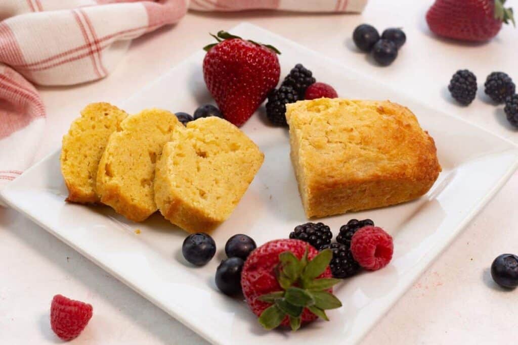 Mini pound cake loaf on square plate sliced with berries.