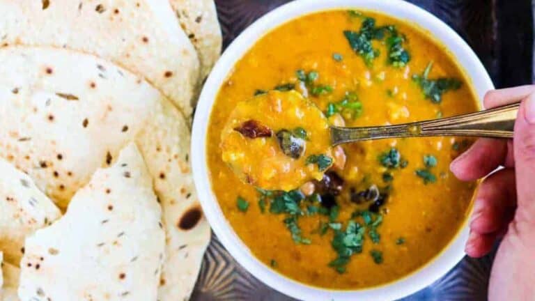 Bowl of mulligatawny soup with a hand lifting a spoonful of soup.