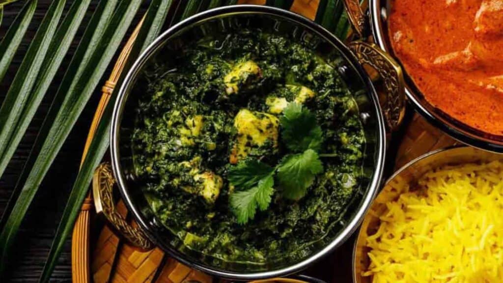 Low angle shot of a bowl of Palak paneer on a fancy silver tray with a fancy silver serving spoon.