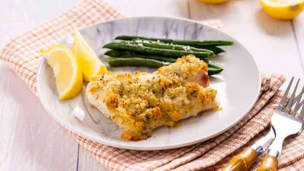 A plate of baked fish with lemon and green beans.