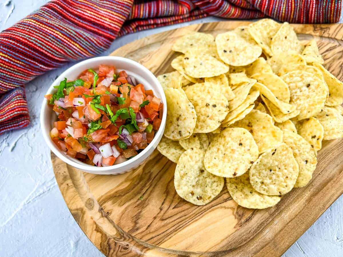A shot of Pico de Gallo on a board with chips nearby.