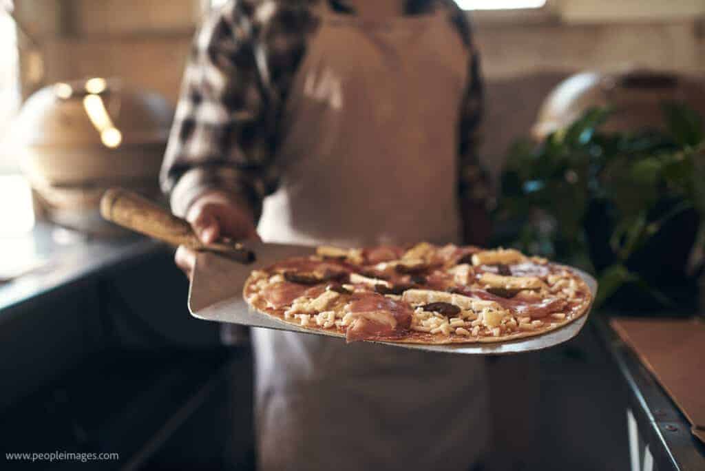 A man is holding a pizza on a tray.