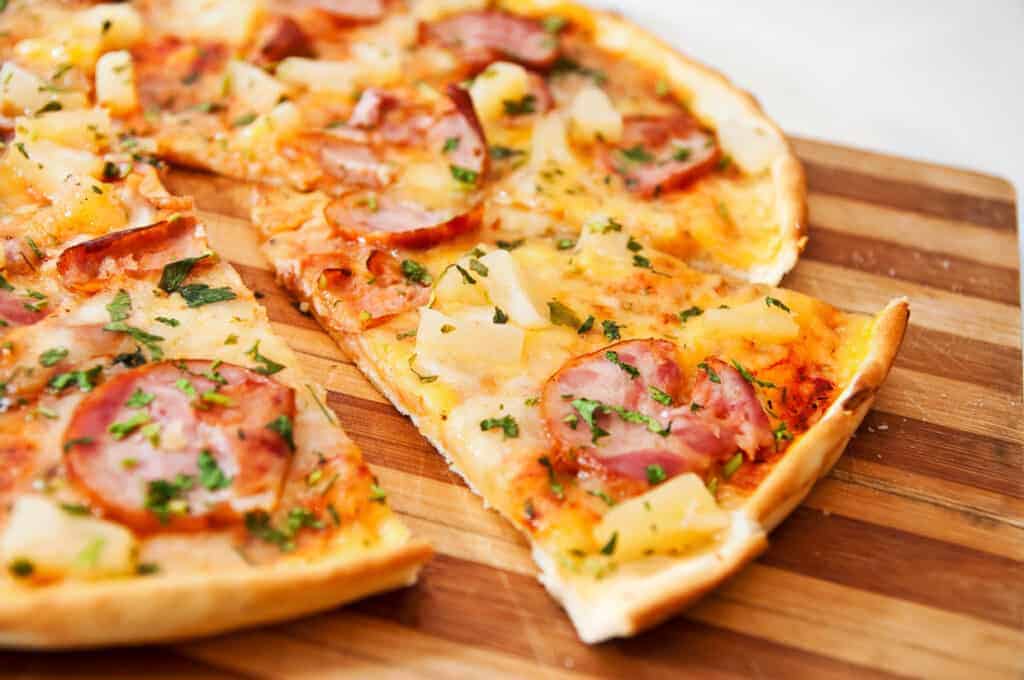 A pizza with ham and pineapple on a wooden cutting board.