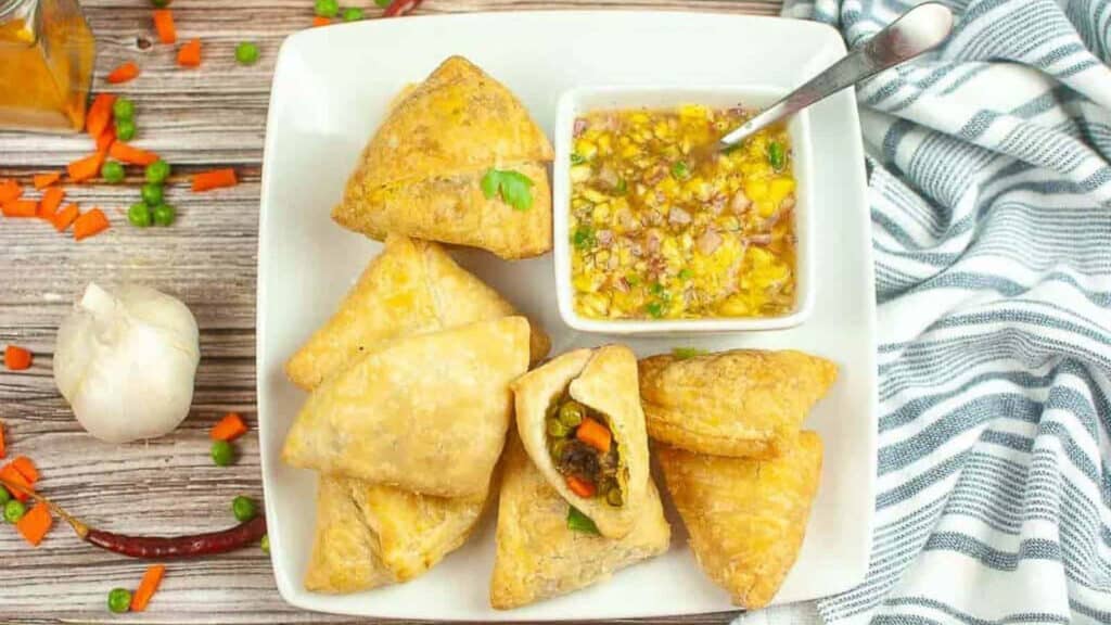 Vegetable samosas on a white plate with dipping sauce.