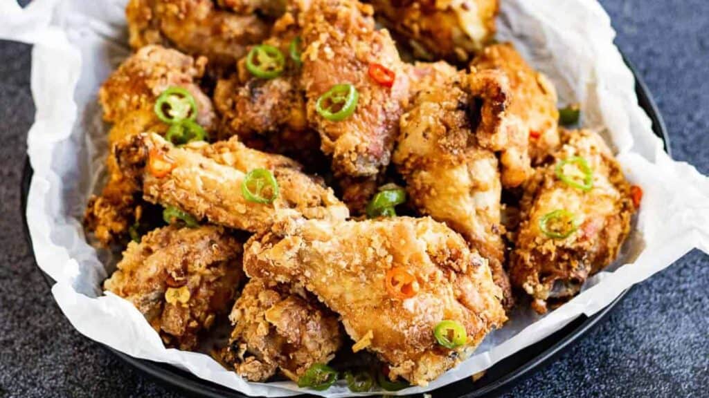 Fried chicken wings in a bowl with green onions.