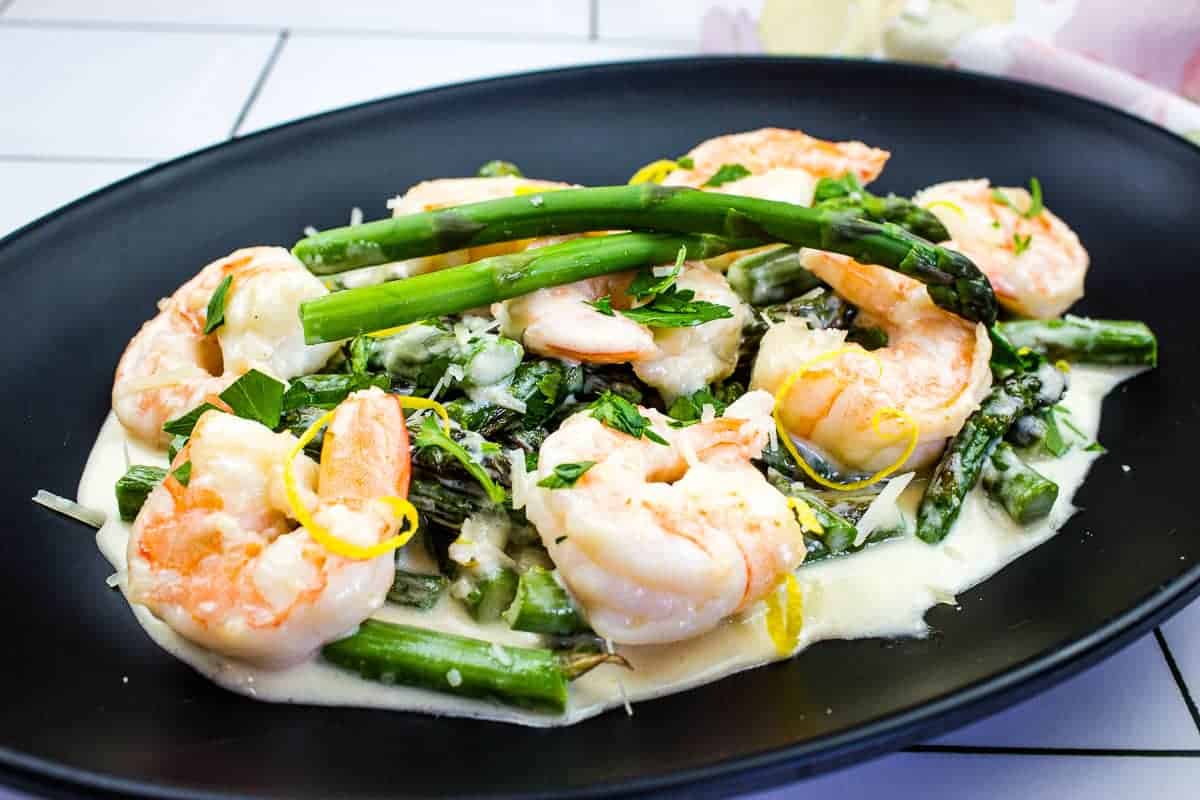 A closeup of Shrimp Alfredo with Asparagus on a black plate.