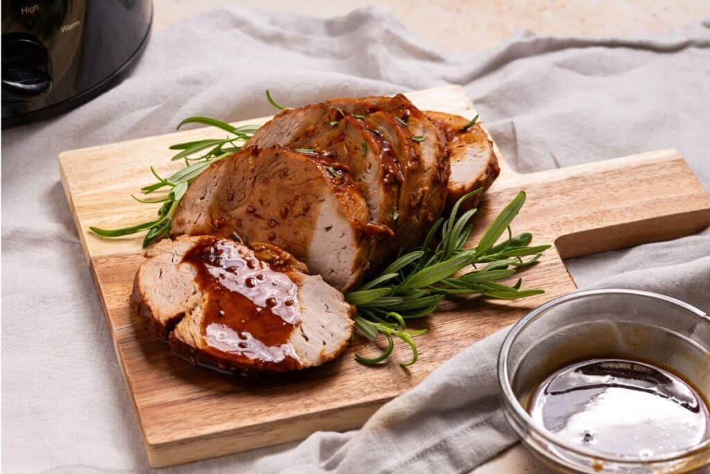 Pork tenderloin on a cutting board next to a slow cooker.