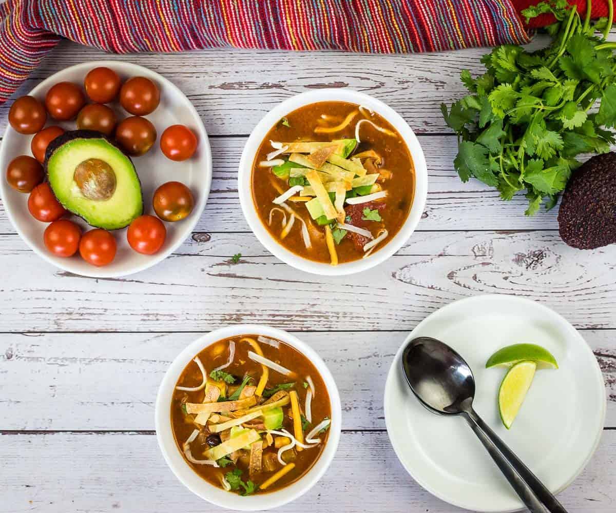 Smoked Chicken Tortilla Soup in two white bowls with garnishes nearby.table.