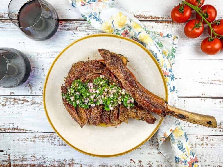 A sliced Tomahawk Steak on a cream color plate.