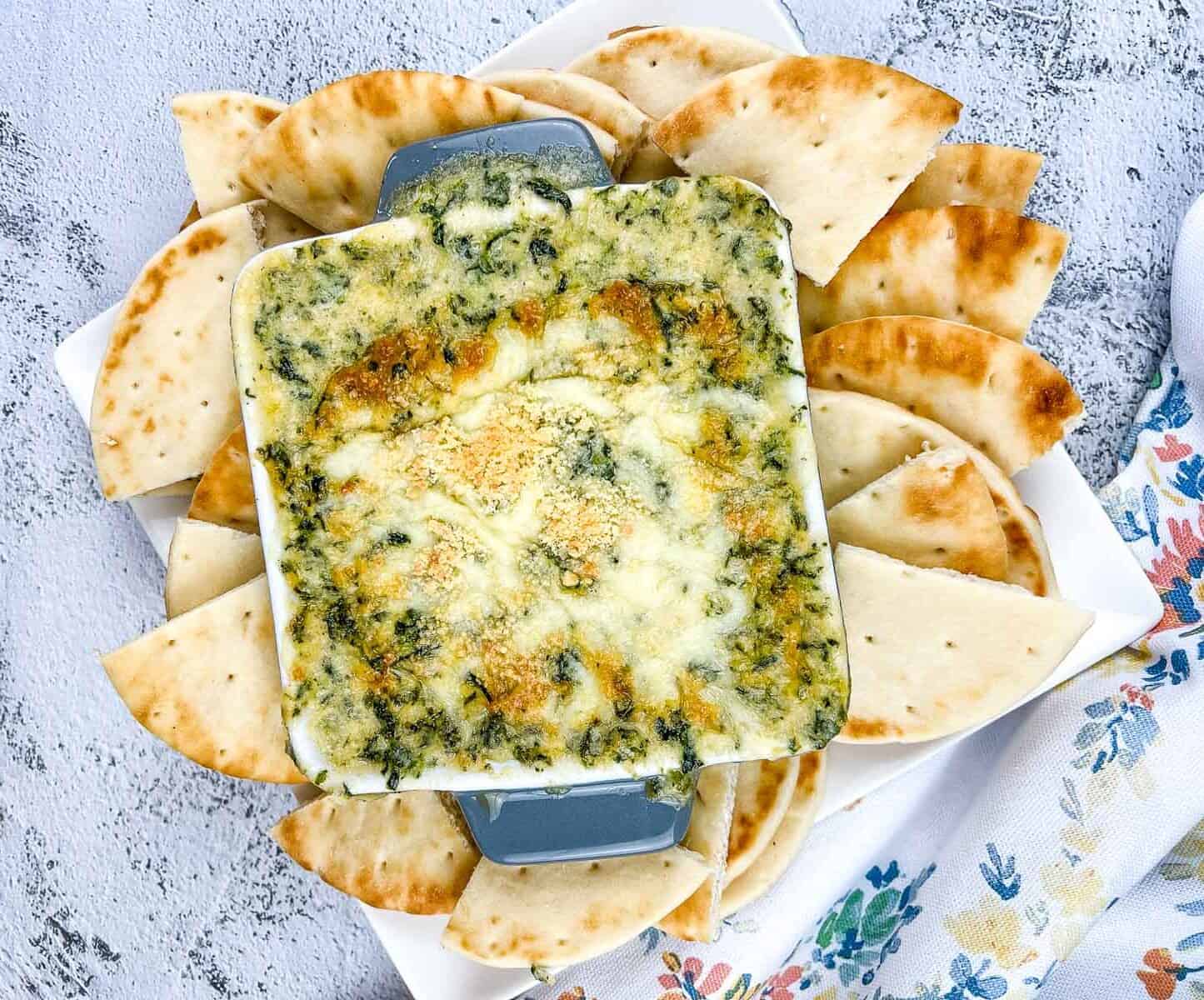 Spinach & Brie Dip in a casserole dish surrounded by pita wedges.