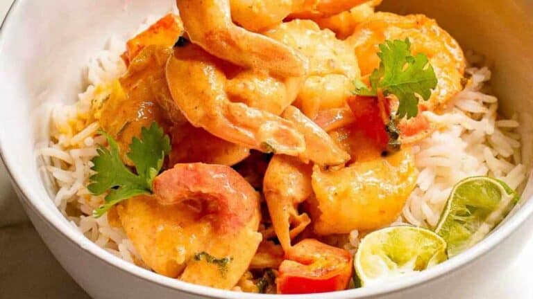 Overhead shot of a bowl of Thai shrimp curry over rice with silverware and lime wedges on the side.