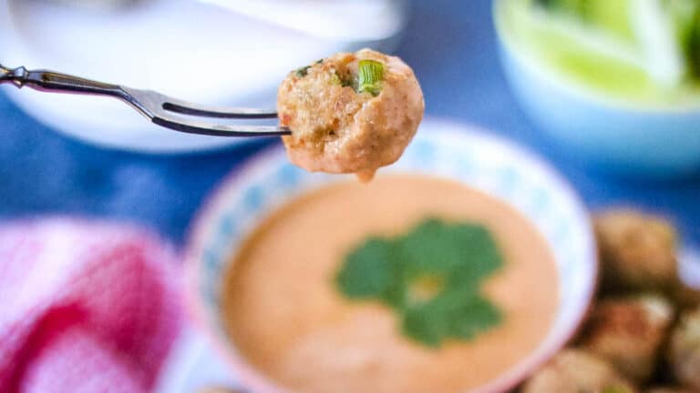 A fork is holding a bowl of meatballs with sauce.