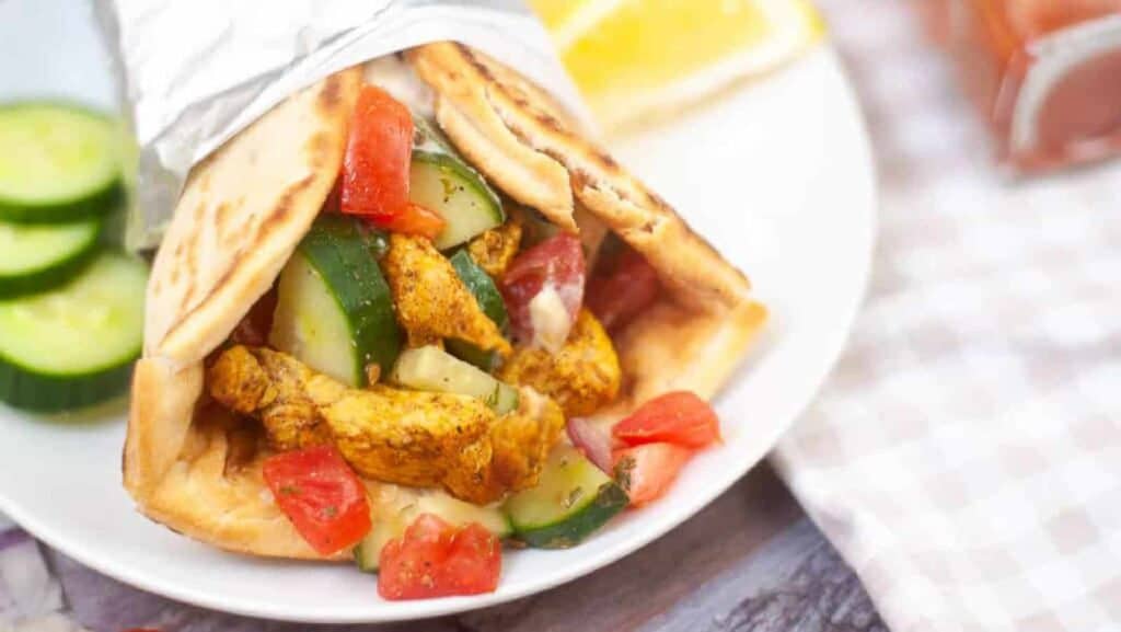 Chicken gyro on a plate with cucumbers and tomatoes.