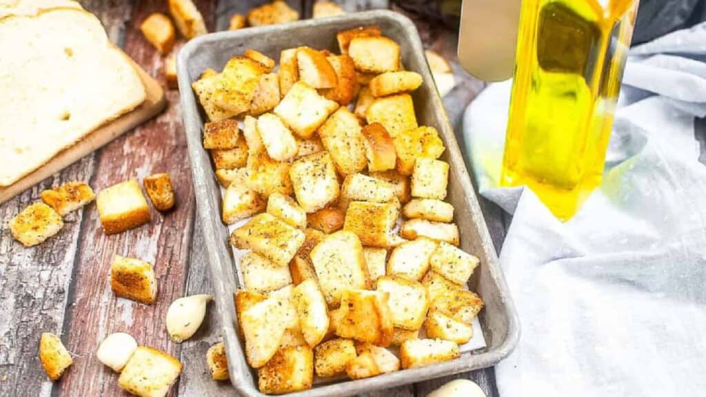 Croutons in a baking dish next to a bottle of olive oil.