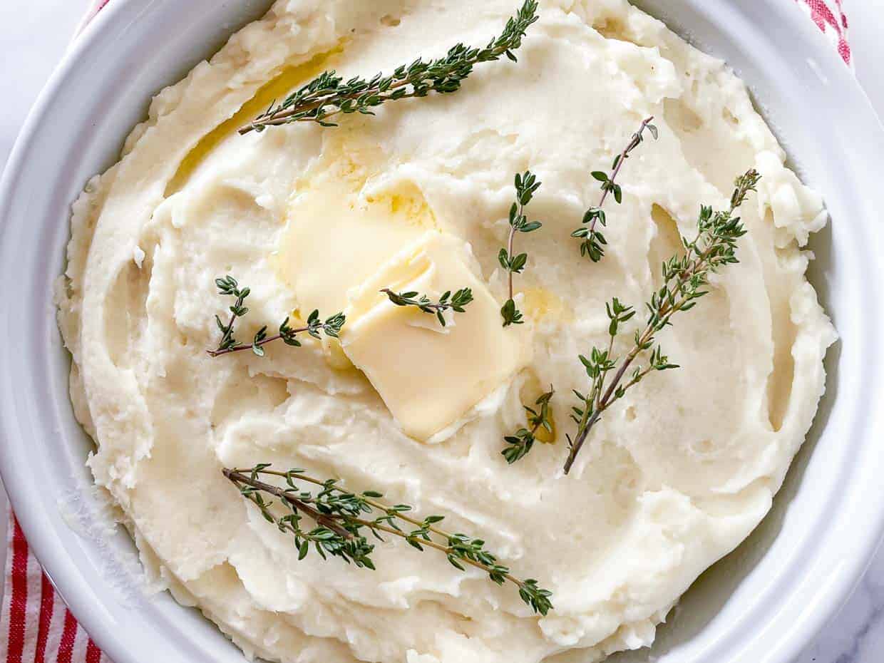A bowl of whipped potatoes with butter and herbs on top.