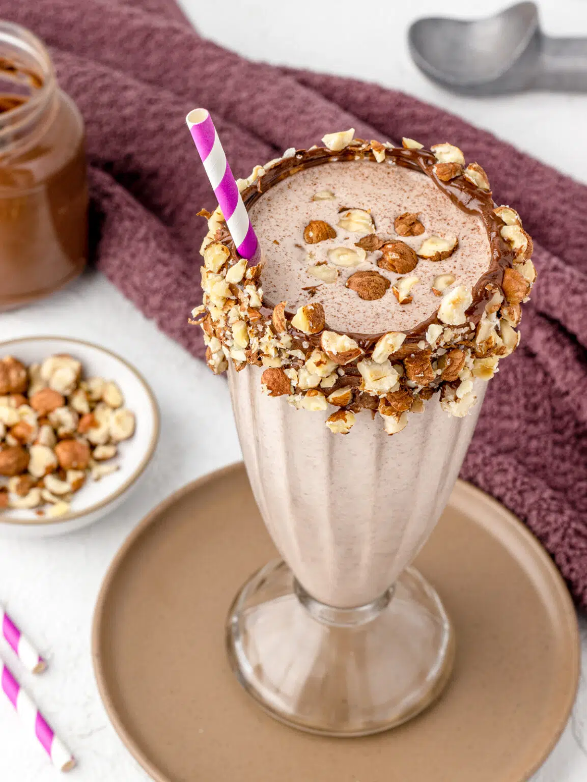 Nutella Milkshake in a tall milkshake glass garnished with a nutella and hazelnut rim and a fun purple straw.