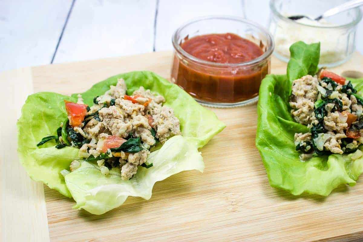Two lettuce wraps with chicken and spinach on a cutting board.