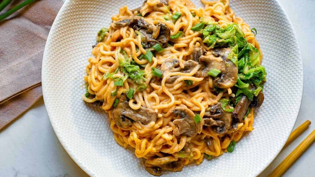 A white plate with noodles and mushrooms on it.