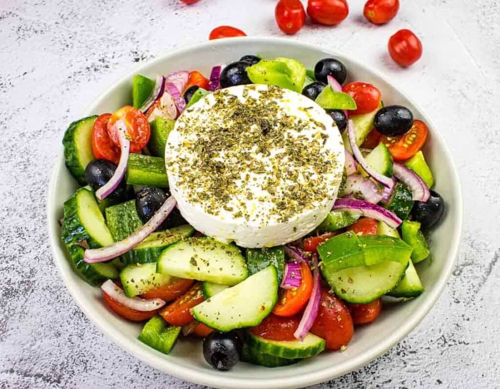 A bowl of greek salad with tomatoes, cucumbers and feta cheese.