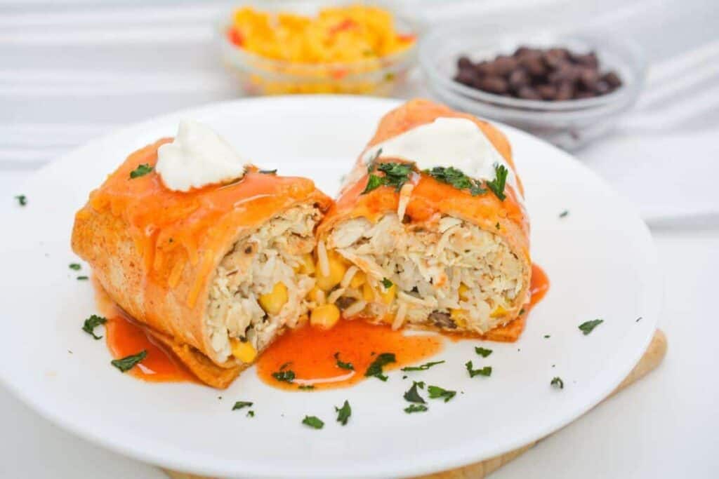 Two chicken enchiladas on a plate with salsa and sour cream.