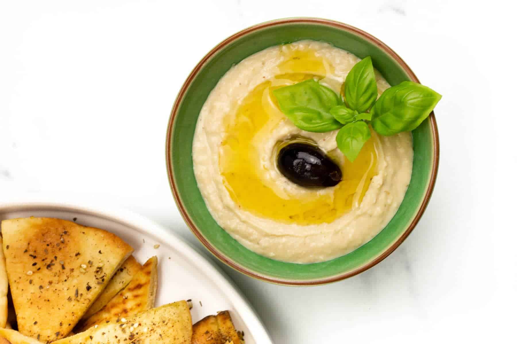A bowl of hummus with pita chips and olives.