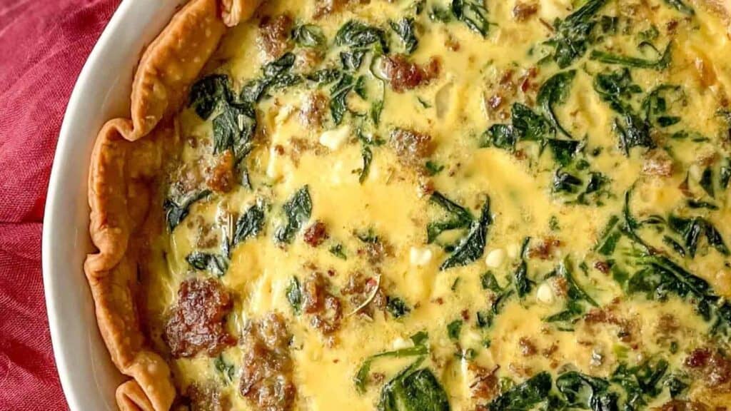 A quiche with spinach and bacon in a white dish.