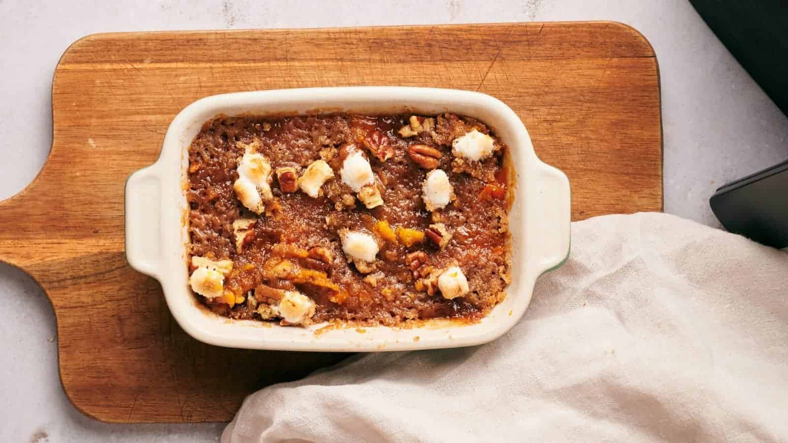 A white dish with a sweet potato casserole on top of a wooden cutting board.