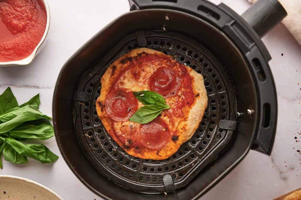 An air fryer with a pizza in it.