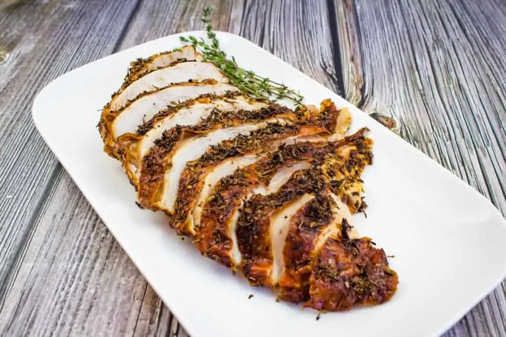 Sliced turkey breast on a white plate with sprigs of thyme.