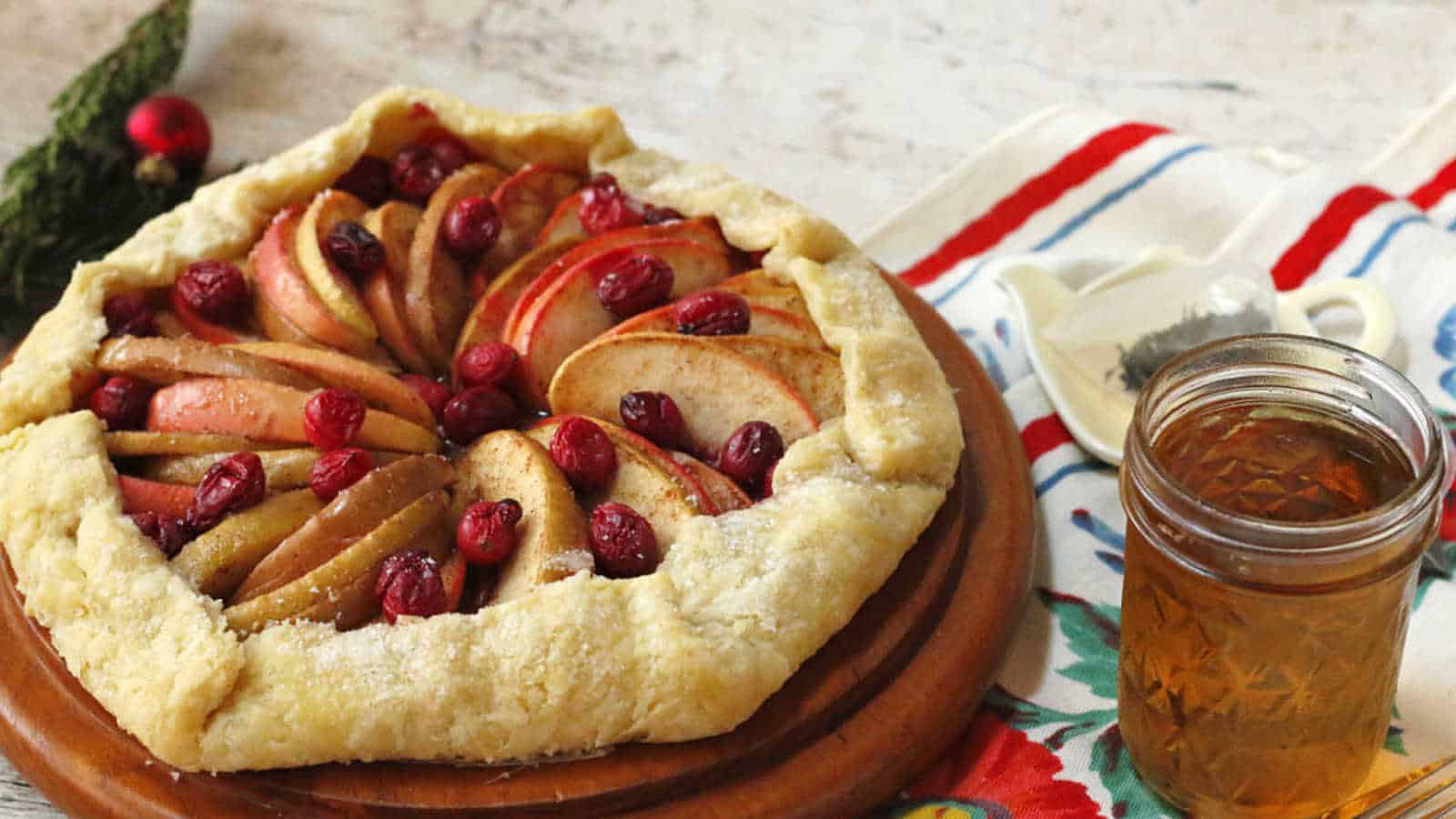 Apple cranberry galette on a wood board with a cup of tea.